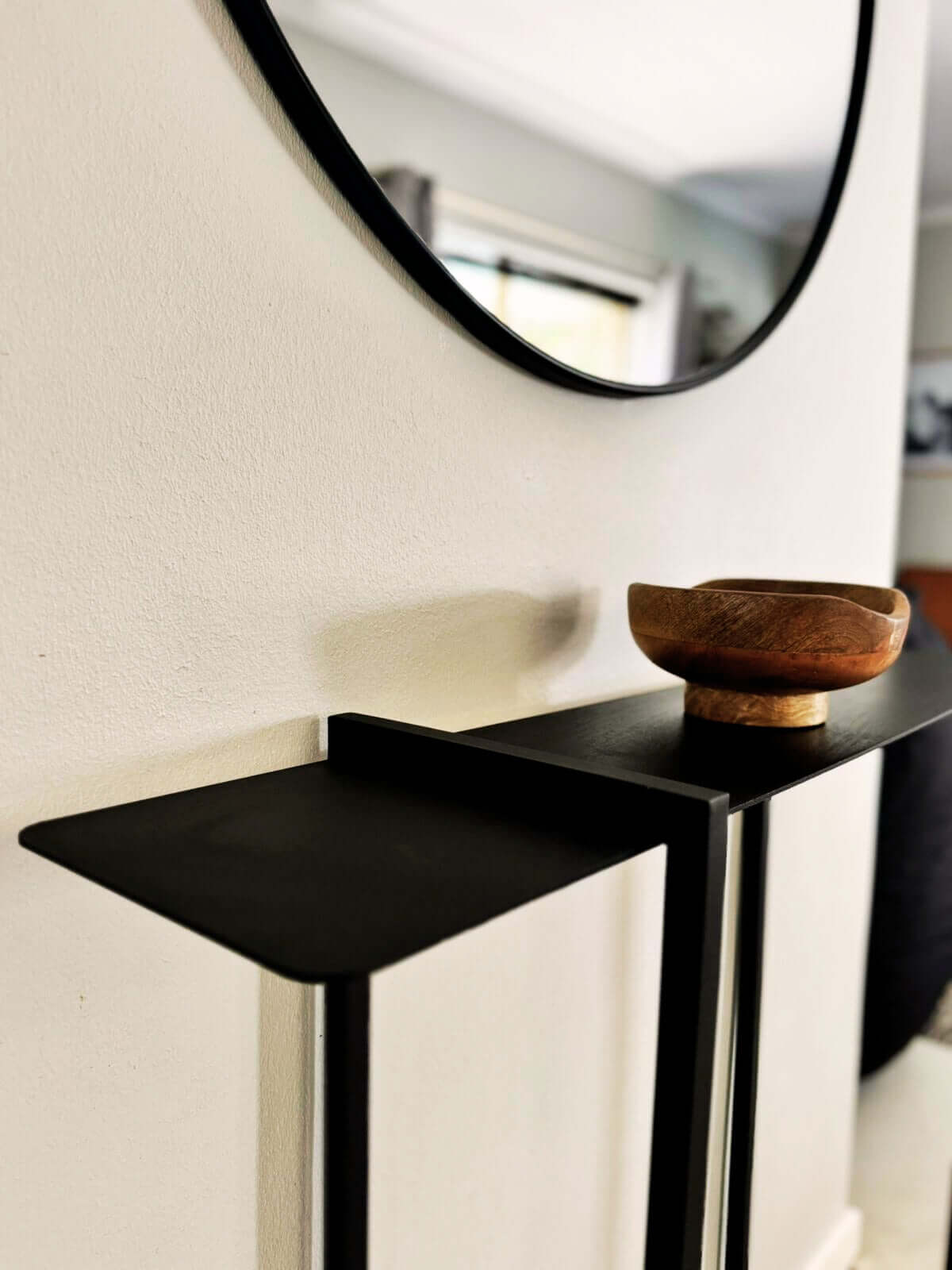 Modern black aluminium console table by Komposite with a wooden decorative bowl and a round mirror.