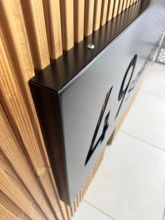 Close-up of a sleek black house sign attached to a wooden wall, showcasing its modern design and quality craftsmanship.