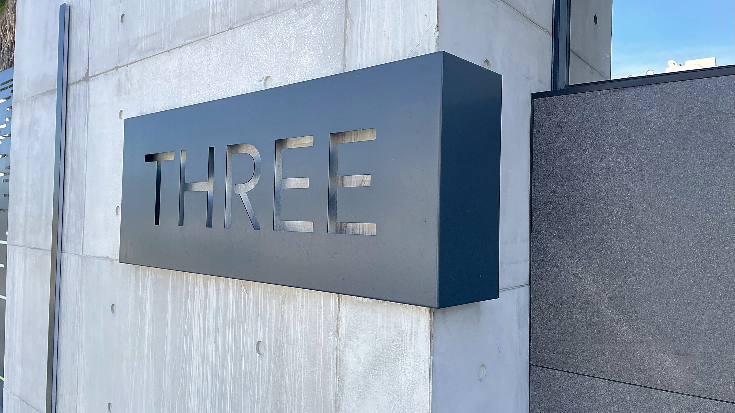 Komposite laser-cut aluminium house sign reading THREE on a concrete wall