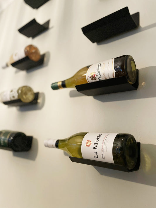 Black aluminium Rakki wine shelves mounted on a wall, each holding a bottle of white wine